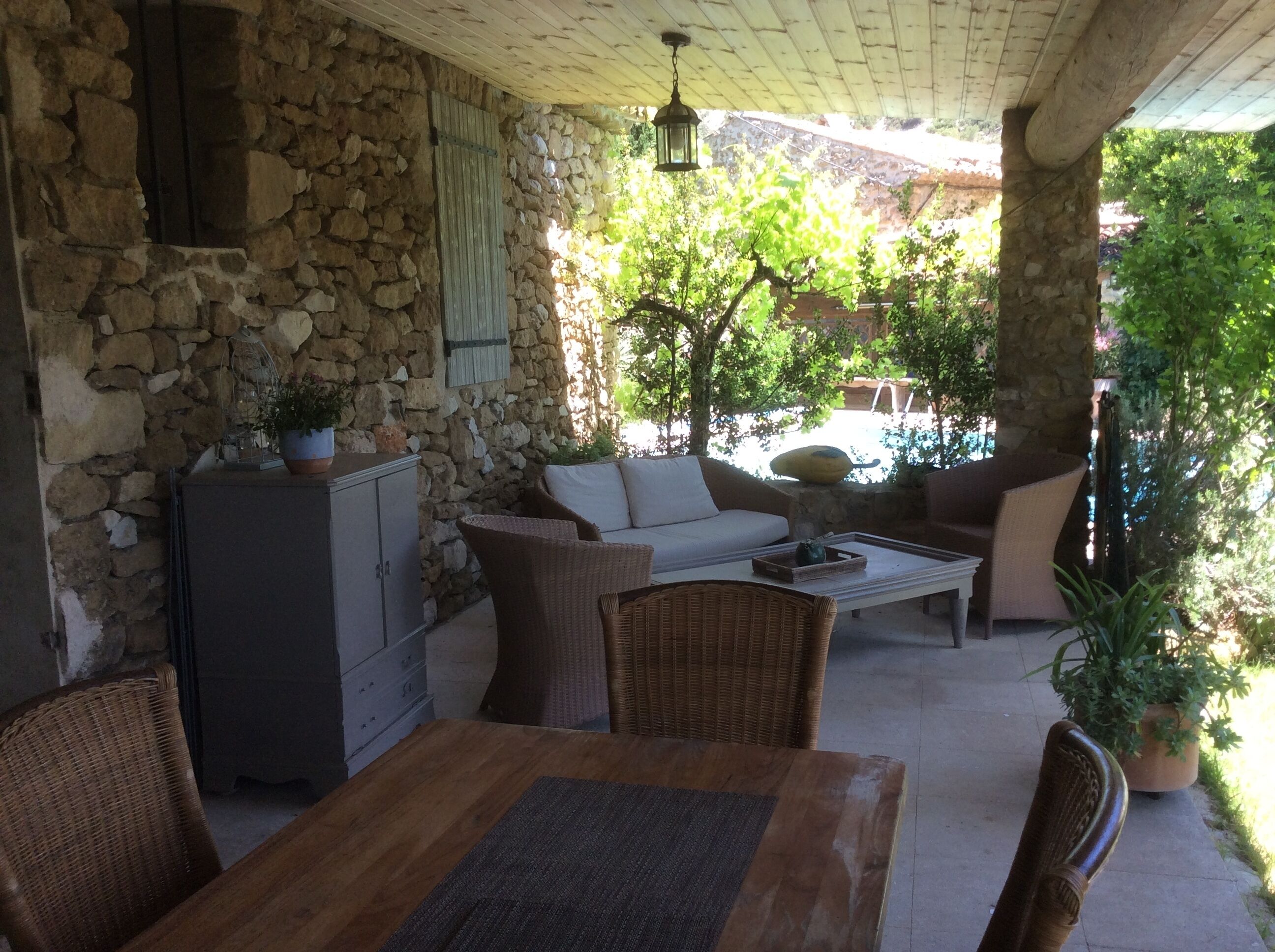 A covered patio with stone walls, wicker furniture, and a table.