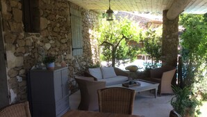 A covered patio with stone walls, wicker furniture, and a table. - SHEEP IN THE REGIONAL PARK LUBERON (Lauris)
