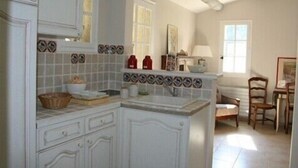 A kitchen with white cabinets, a tiled backsplash, and a dining area with a table and chairs. - SHEEP IN THE REGIONAL PARK LUBERON (Lauris)