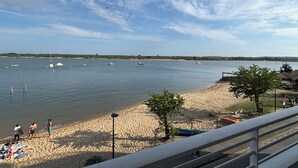 Ein Strand mit Booten auf dem Wasser, Personen im Sand und einem klaren Himmel.