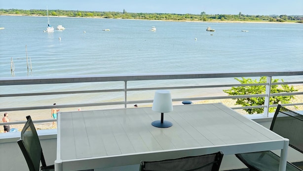 Ein Balkon mit Tisch und Stühlen mit Blick auf ruhiges Wasser und Boote.