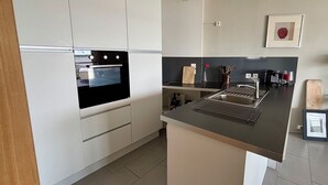 Eine moderne Küche mit weißen Schränken, einem eingebauten Backofen, einer Edelstahl-Spüle und einer kleinen Kochinsel mit Schneidebrett.