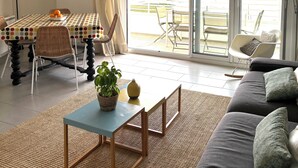 Ein Wohnzimmer mit Essbereich, einer Couch, einem Tisch mit Pflanze und Blick durch große Fenster.