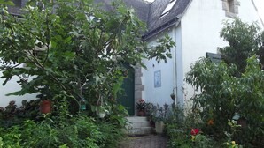 Een smal pad van baksteen dat leidt naar een wit gebouw met een groene deur en een blauw plaquette.