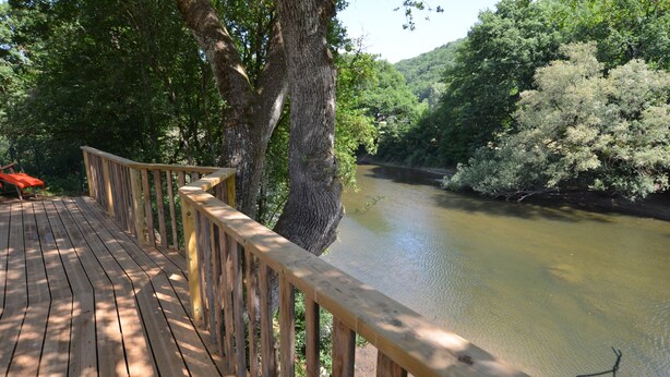 Una terraza de madera con vista a un río, rodeada de árboles.
