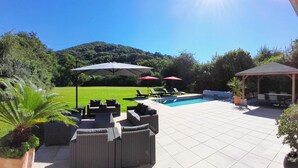 Un patio trasero con piscina, sillas de descanso y un pabellón.
