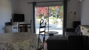 A room with a bed, a dining table, a sofa, and a small table. There is a TV on a stand and a window with a view of trees. - Gîte de provence jacuzzi (Velleron)