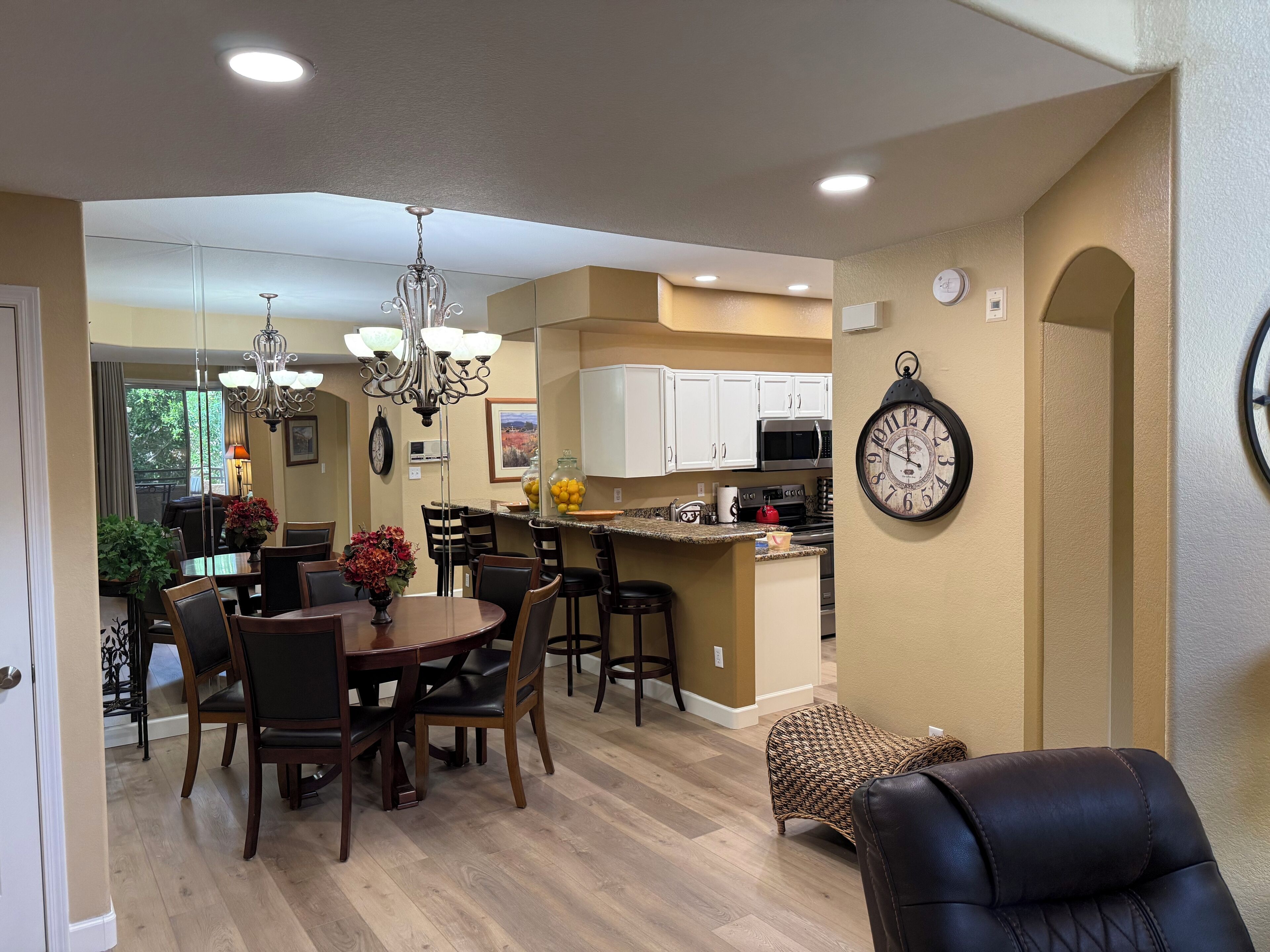 A spacious dining area with a chandelier, a kitchen with white cabinets, and a clock on the wall.