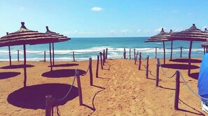 Una playa con sombrillas de paja y una barrera de cuerda.
