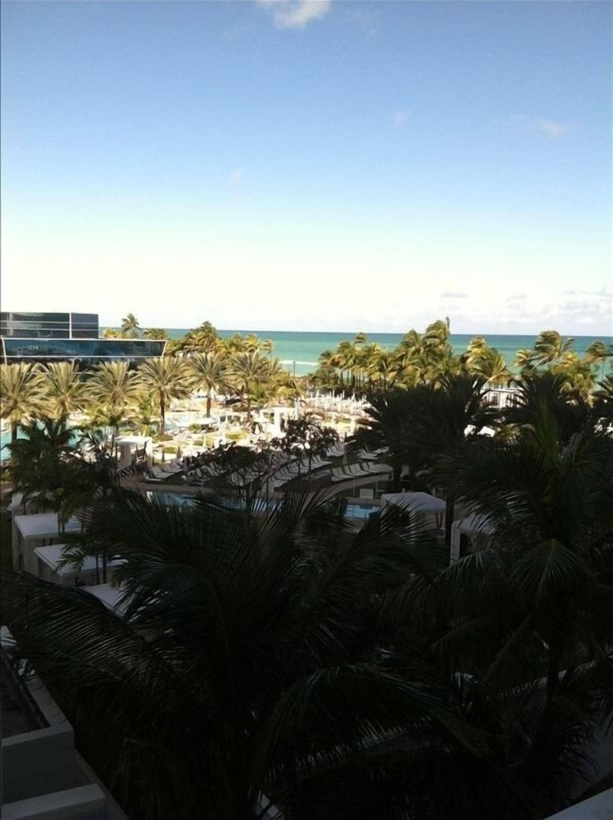 A resort with a pool area surrounded by palm trees and a view of the ocean.
