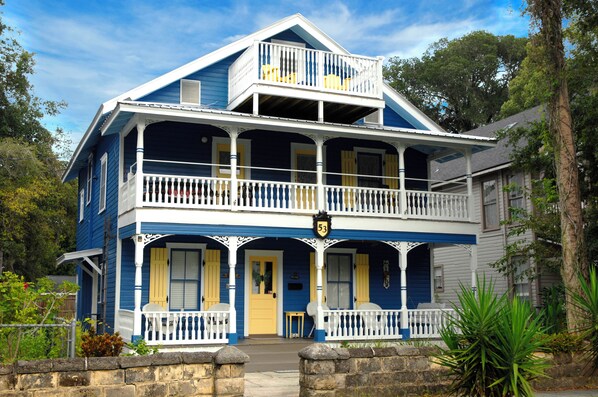 A two-story house with a balcony, a front porch, and a stone wall in front.