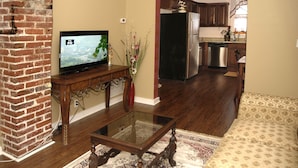 Una sala de estar con televisor, una mesa de centro de madera, sofá y una zona de cocina con refrigerador y estufa.