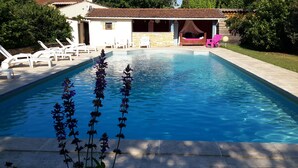 Ein rechteckiger Swimmingpool mit klarem, blauem Wasser, umgeben von weißen Liegestühlen und einem Gebäude mit rotem Ziegeldach.