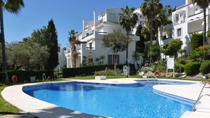 A swimming pool with a clear blue water, surrounded by a white pool deck, palm trees, and a building with balconies in the background. - LARGE PENTHOUSE 3 20-6 SEA VIEW SWIMMING POOL GARDEN CALAHONDA RIVIERA DEL SOL  (Mijas)
