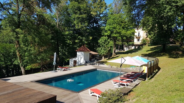 Une piscine avec une terrasse en bois, des chaises longues et un petit bâtiment.