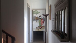 Un couloir avec un escalier en bois sur la gauche, un lampadaire et un tableau sur le mur de droite.