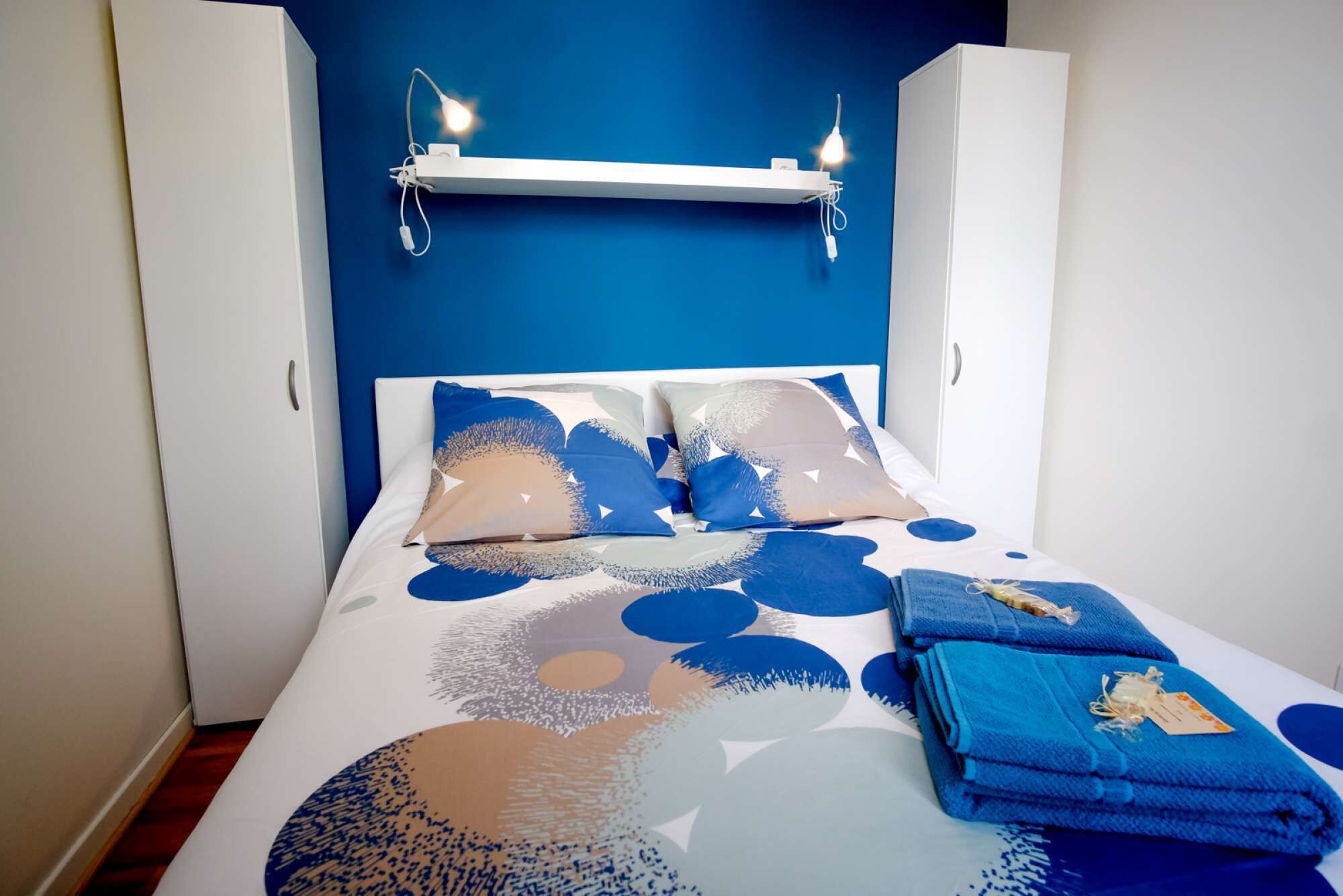 A bed with a blue and white patterned bedspread, two pillows, and a stack of blue towels.