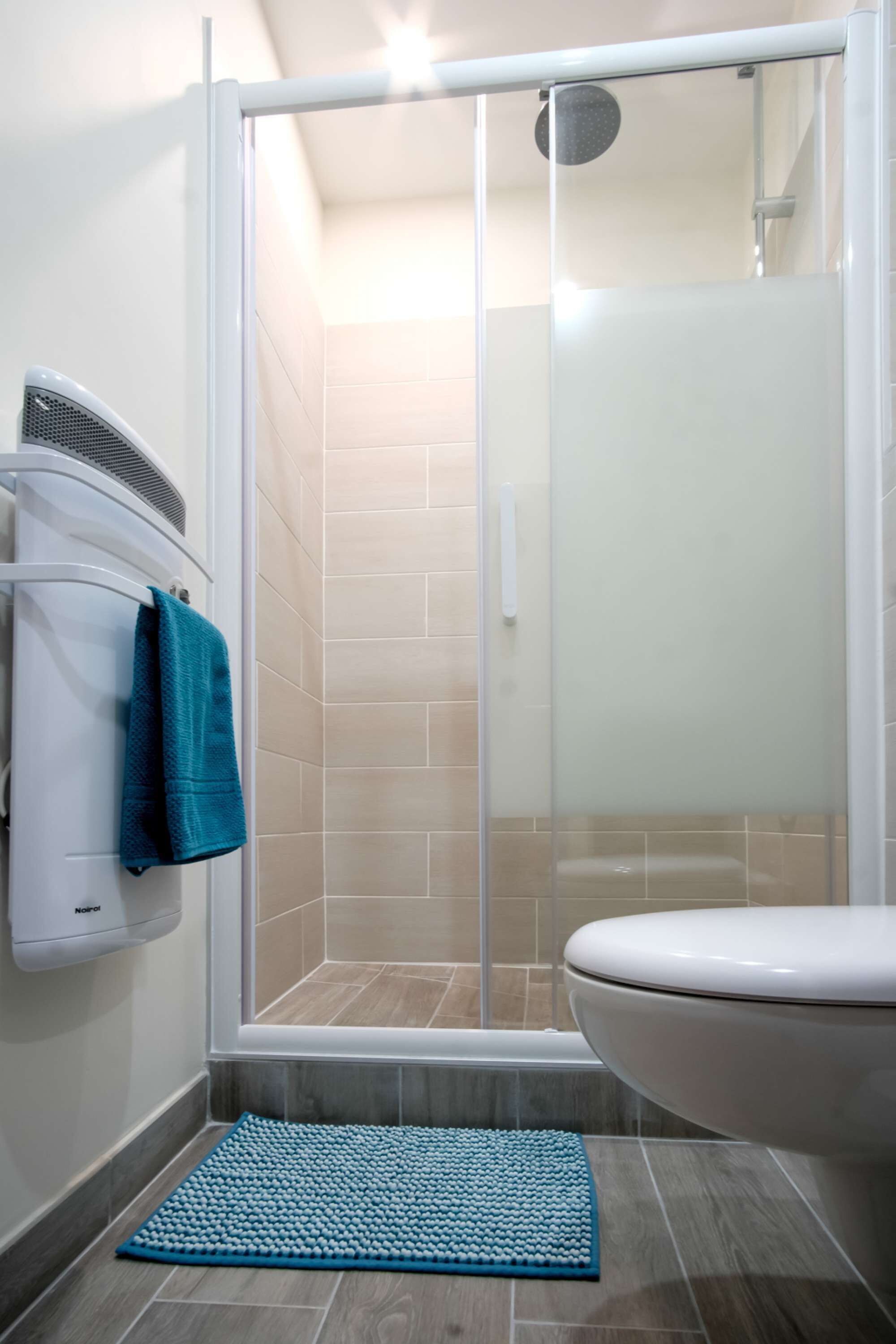 Une salle de bain comprenant un espace douche, des toilettes et un porte-serviettes avec une serviette.