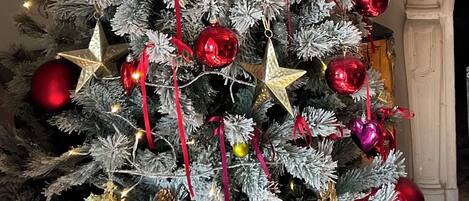 Een kerstboom met rode en gouden versieringen, voor een witte bakstenen muur en een open haard.