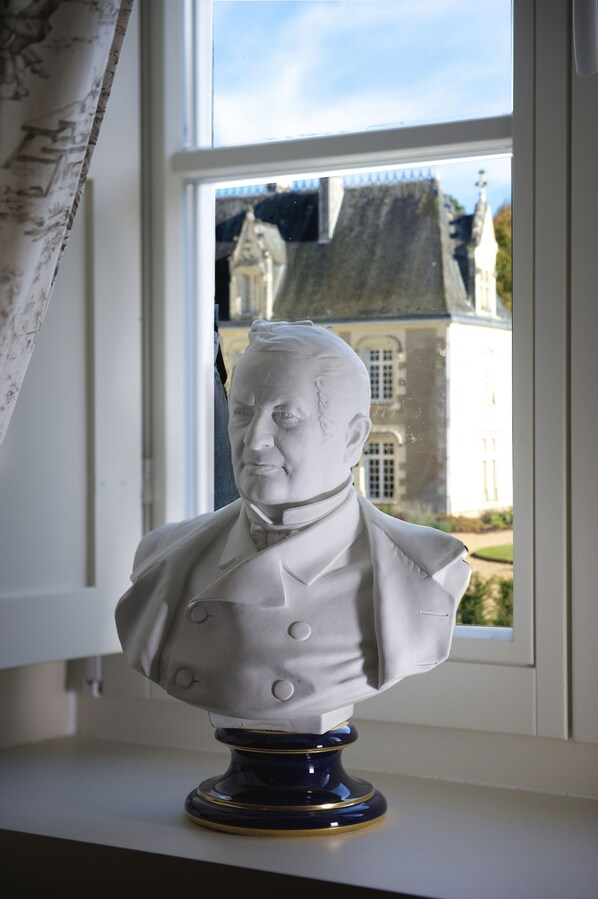 A bust sculpture on a pedestal by a window with a view of a building. - House 14 people in the castle of Beauvais (Azay-sur-Cher)