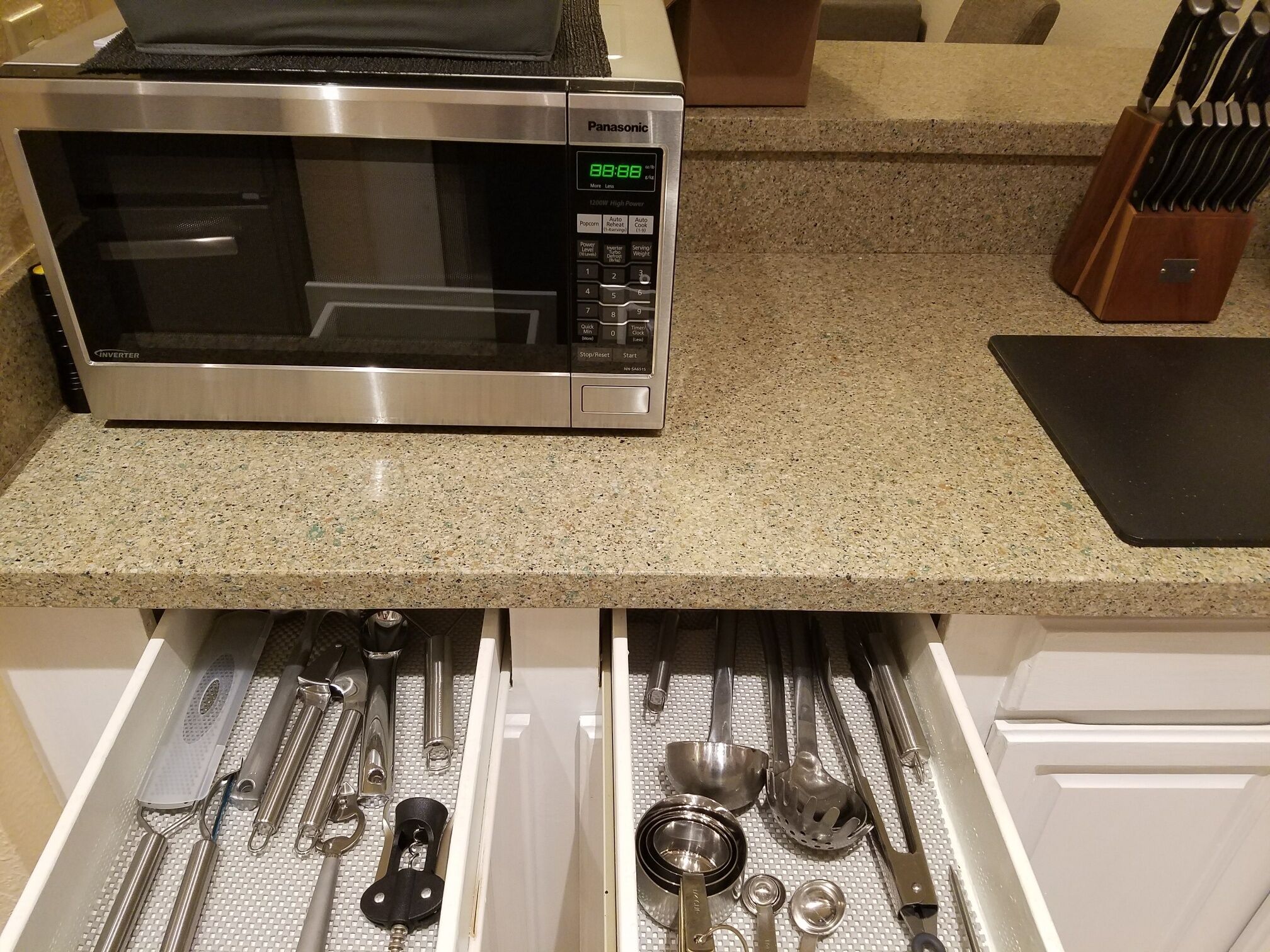 A kitchen with a microwave oven on the countertop and a drawer below containing various kitchen utensils.