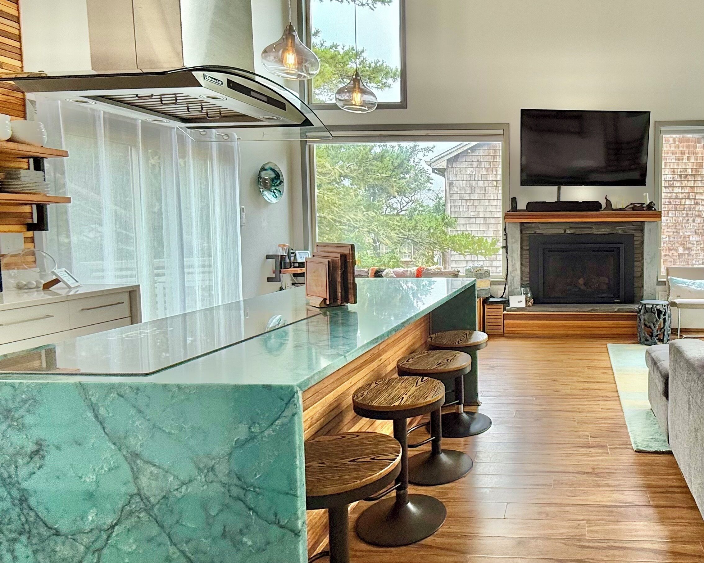 Una cocina moderna con una isla de mármol, taburetes de bar, chimenea y un televisor grande.