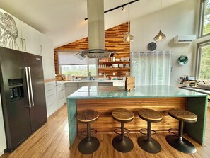 Una cocina moderna con una isla central, taburetes de bar y una pared decorativa de madera.
