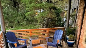 A deck with four blue Adirondack chairs, a square fire pit, and a wooden railing.