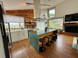 A modern kitchen with a marble island, wooden flooring, and a built-in TV.