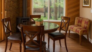 Un comedor con una mesa redonda, cuatro sillas, una pared de acento de piedra, un ventanal con vistas a árboles y una chimenea.