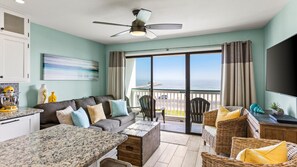 A spacious living area with a large window, a ceiling fan, a kitchen area with a mixer, and a flat-screen TV. - Top Floor! Oceanfront View, Heated Pool, Casa Del Mar! (Galveston)