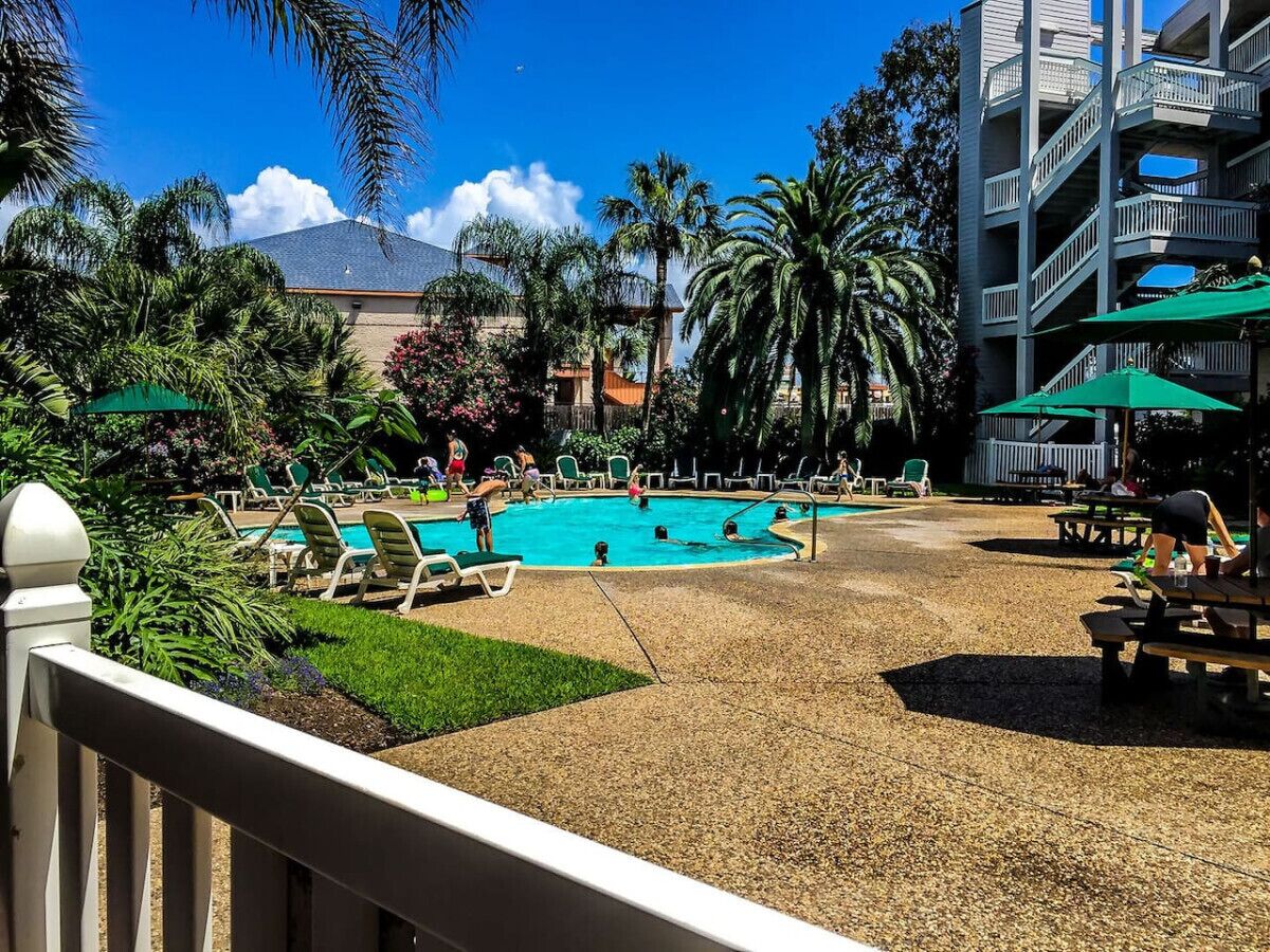Un espace piscine avec des chaises longues, une piscine et un bâtiment doté de balcons.