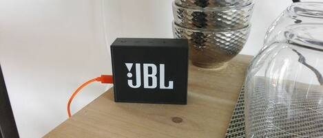 A black JBL speaker on a wooden surface with a woven mat beside it.