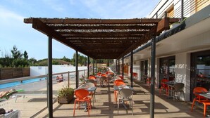 Un espacio de estar al aire libre techado con sillas y mesas naranjas, con vista a una piscina.