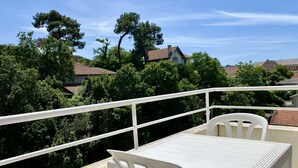 Varanda com mesa e cadeiras brancas, cercada por árvores e casas ao fundo.
