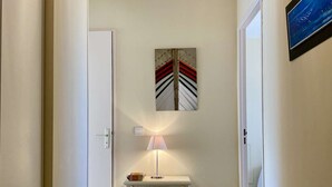 Um corredor com uma porta branca, uma escrivaninha com uma lâmpada e um quadro na parede.
