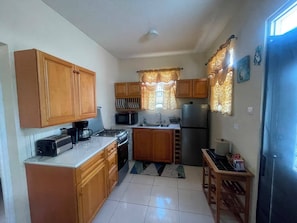A compact kitchen with wooden cabinets, a gas stove, a microwave, a refrigerator, and a sink.