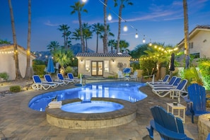 A swimming pool with lounge chairs and a hot tub, surrounded by palm trees and string lights.