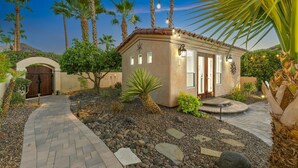 A small building with a tiled roof, a stone pathway, and a palm tree in the foreground. - California Paradise: #231868 3BR Pool, Spa, BBQ! (La Quinta)