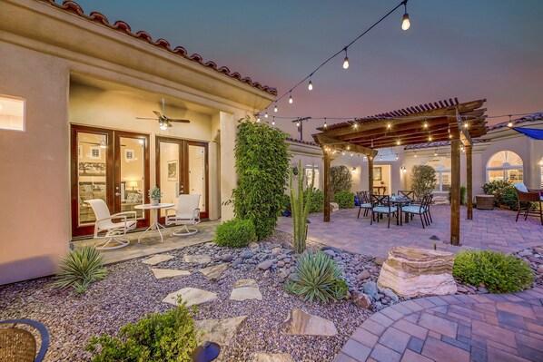 Un patio con mobiliario exterior, una pérgola y un jardín con rocas y plantas.