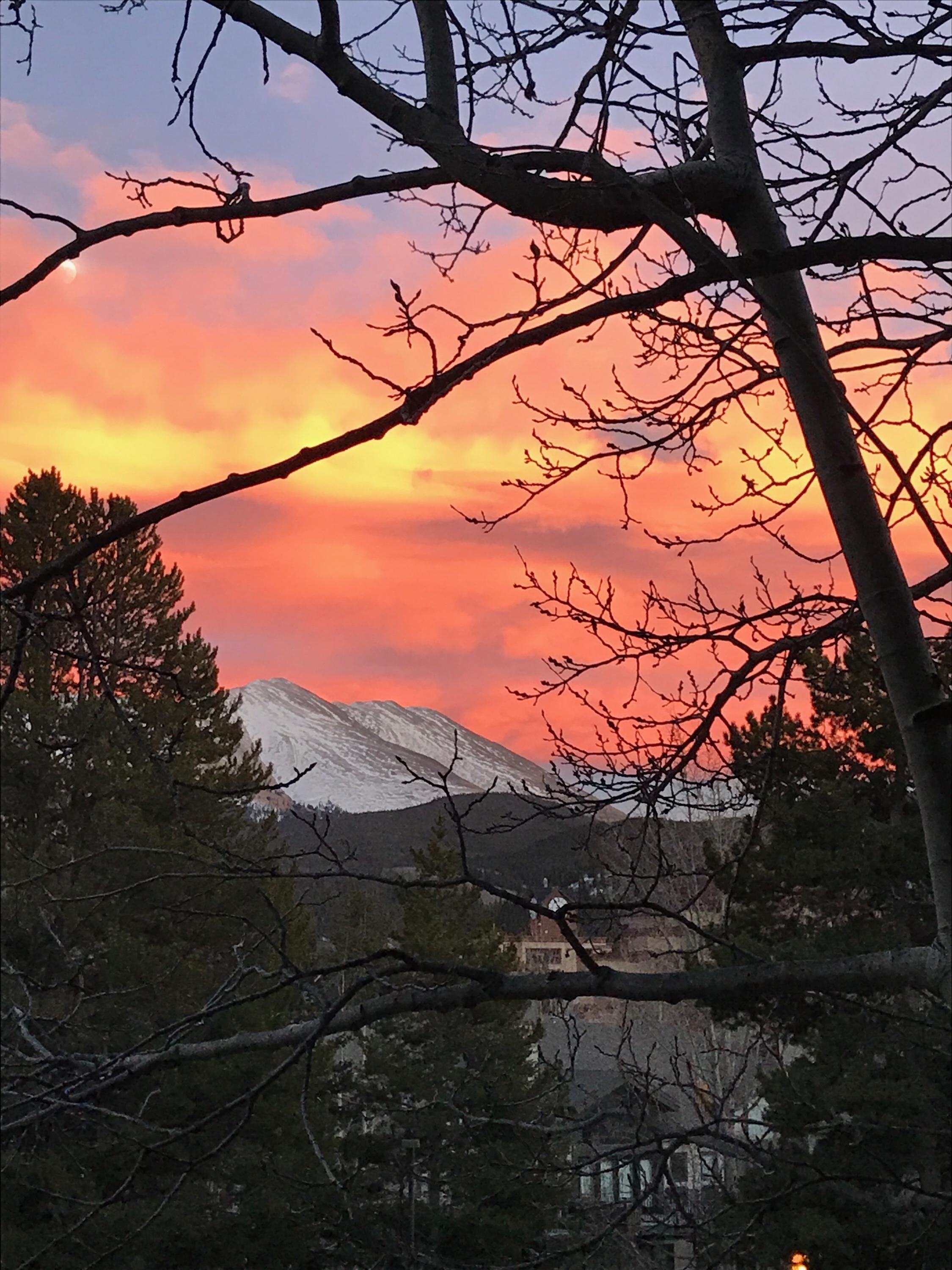 A mountain with a sunset in the background, surrounded by trees and buildings.