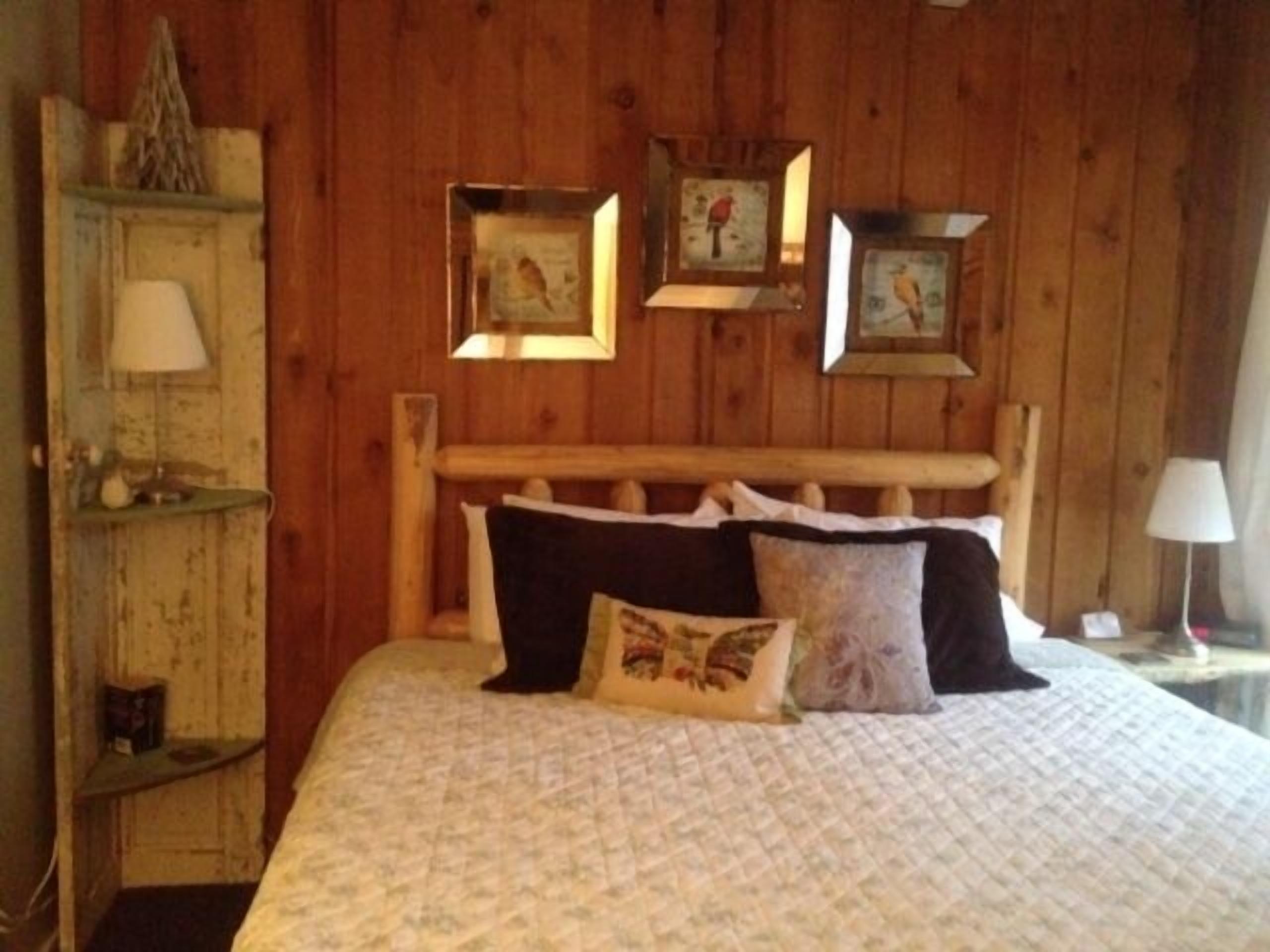 Una habitación con paneles de madera, una cama, una mesita de noche y un estante con una lámpara.