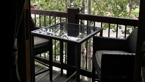 Een houten terras met een glazen tafel en stoelen, omringd door bomen en uitzicht op de straat.
