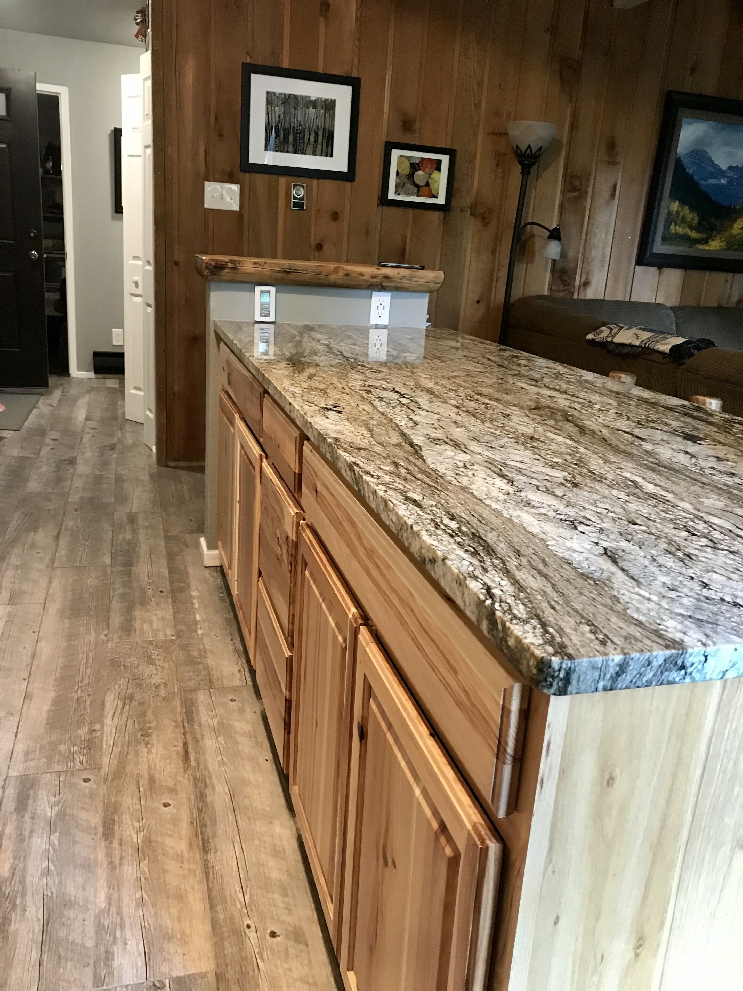 Una cocina con armarios de madera, encimera de granito y suelo de madera.