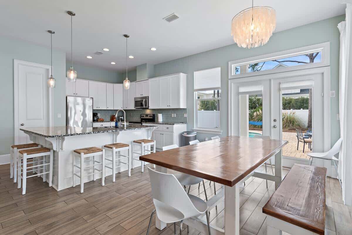 A modern kitchen with white cabinetry, a central island with stools, pendant lighting, and a view to an outdoor area.