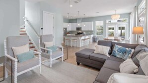 Ein modernes Wohnzimmer mit grauem Sofa, weißen Sesseln und einer Treppe, die in einen Küchenbereich führt.