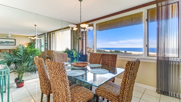 Een eetgedeelte met een glazen tafel, rieten stoelen en uitzicht op de oceaan.