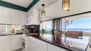 Een moderne keuken met witte kasten, een zwart aanrecht en een groot eiland. Er is uitzicht op de oceaan door grote ramen.
