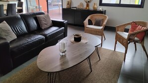 A modern living room with a black leather sofa, a round wooden coffee table, and a wicker chair.
