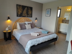 Un dormitorio con cama, lámparas de noche, una obra de arte en la pared, un cuadro enmarcado y un baño visible a través de una puerta abierta.